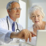 White male doctor and older white female patient look at a computer screen