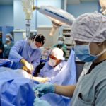 3 people in surgical scrubs surround an operating room table.